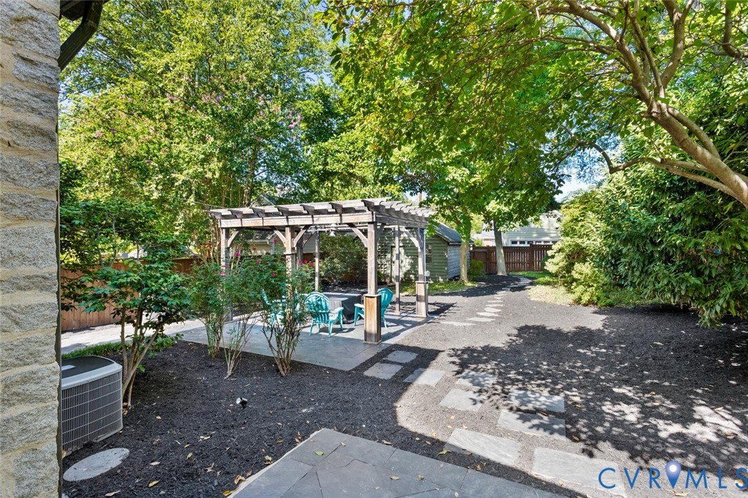 Expansive outdoor space featuring a wood pergola, stone-finish patio, stepping stone pathway, and mature trees