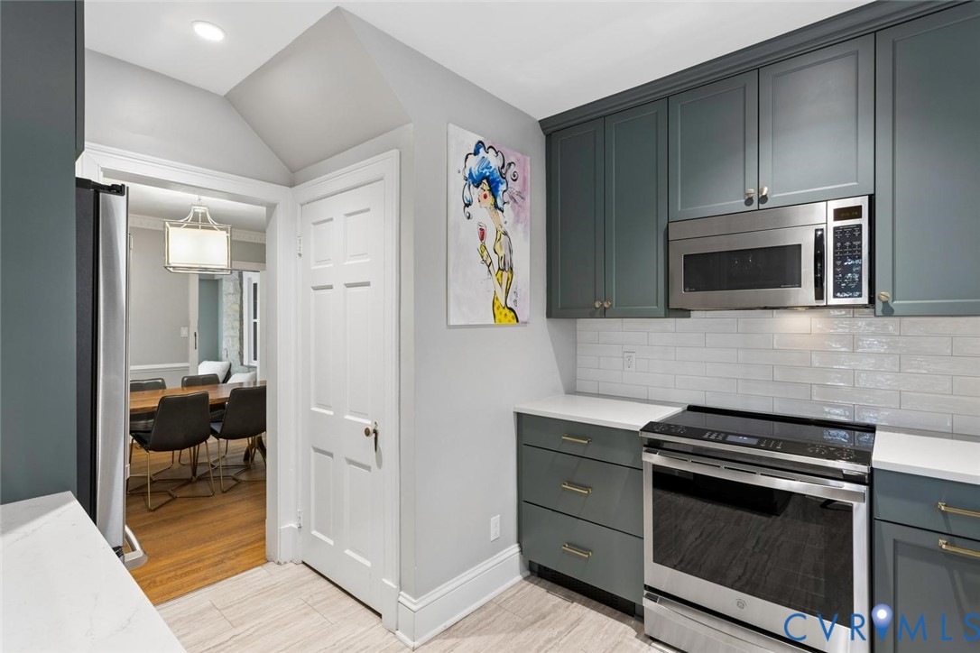 Modern kitchen featuring integrated stainless steel appliances, white subway tile backsplash, light-toned countertops, and deep-toned cabinetry with gold-finish hardware
