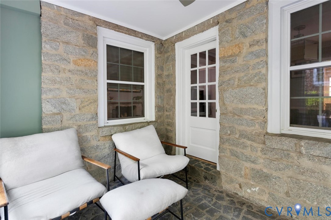Stone-clad exterior wall, single-pane window with white trim, white French door, and stone paver flooring