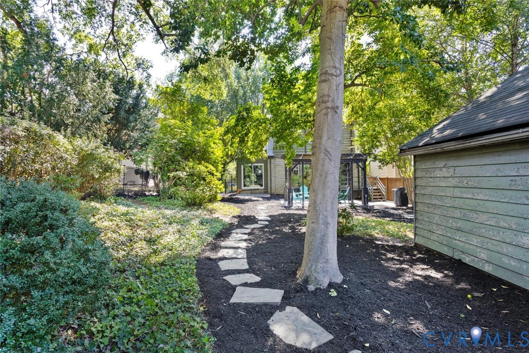 Mature trees, stepping stone pathway, extensive ground cover, and a detached structure with siding