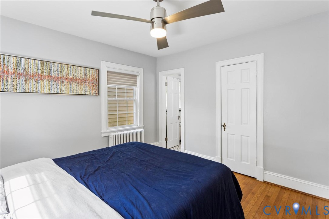 Hardwood flooring, multi-pane window with blinds, ceiling fan with integrated lighting, white paneled door, and radiator