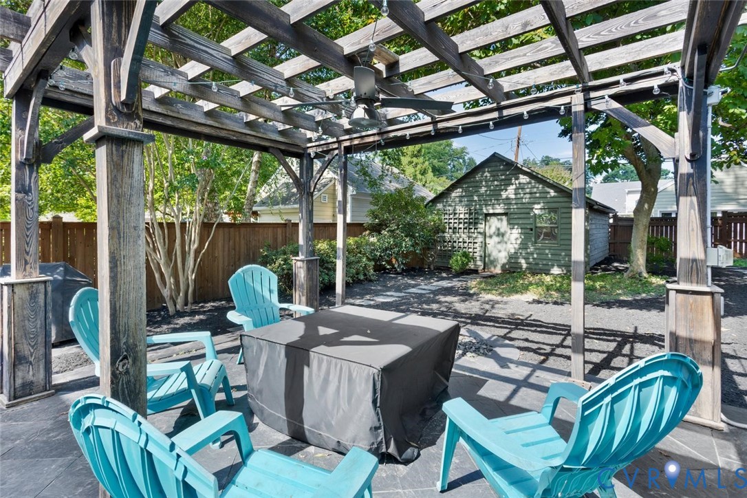 Sophisticated outdoor entertaining space featuring a slatted pergola with integrated overhead structure, concrete patio flooring, and multiple Adirondack-style seating arranged around a fire table with dark fabric cover