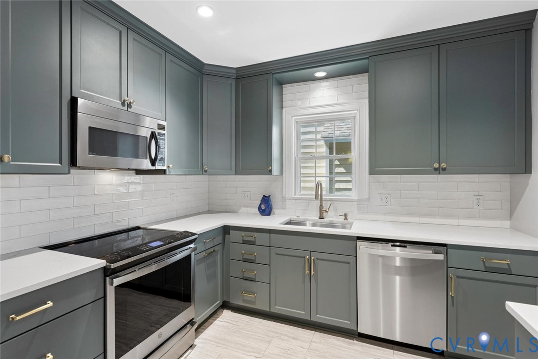 Kitchen featuring gray shaker-style cabinetry, white countertops, subway tile backsplash, and stainless steel appliances