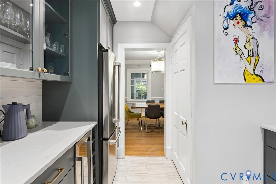Stainless steel refrigerator, white subway tile backsplash, white countertops, dark cabinetry, and gold-tone hardware