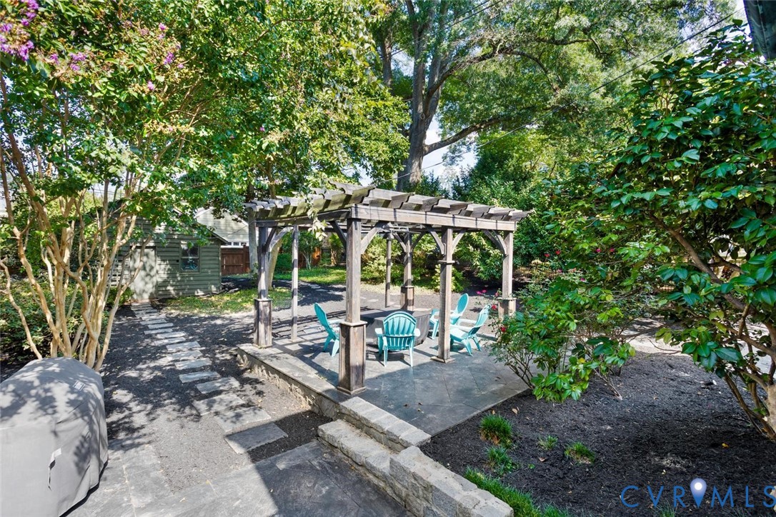 Expansive patio featuring a wooden pergola, stone paver steps, and a stone retaining wall