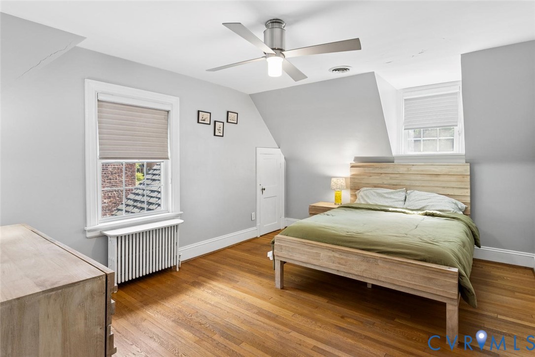 Hardwood flooring throughout, featuring a ceiling fan with integrated lighting, and multiple windows with blinds