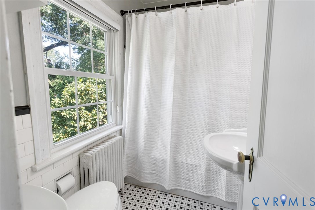 Bathroom featuring a pedestal sink, black and white floor tiles, white subway tile wainscoting, and a multi-pane window