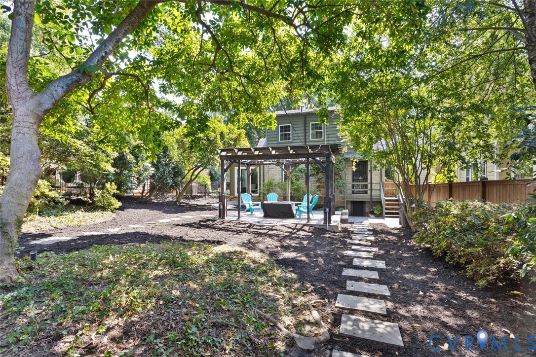 Expansive backyard featuring mature trees, a stone paver path, a dedicated patio with a pergola, and a privacy fence