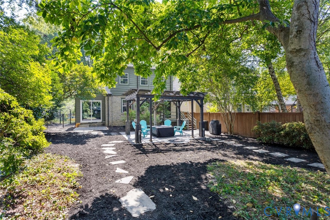 Expansive backyard featuring a stone patio, a wooden pergola structure, a privacy fence, and a stone paver pathway