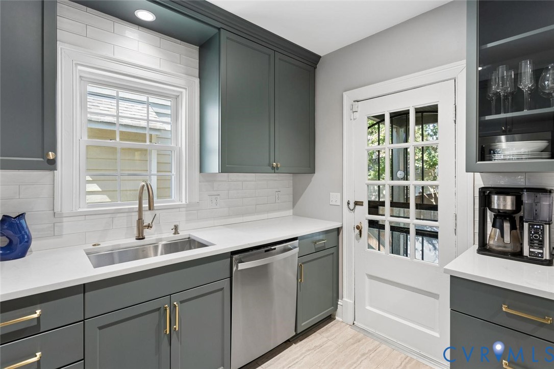 Custom cabinetry with gold-tone hardware, white countertop, stainless steel sink with a gooseneck faucet, white subway tile backsplash, and a glass-paned door