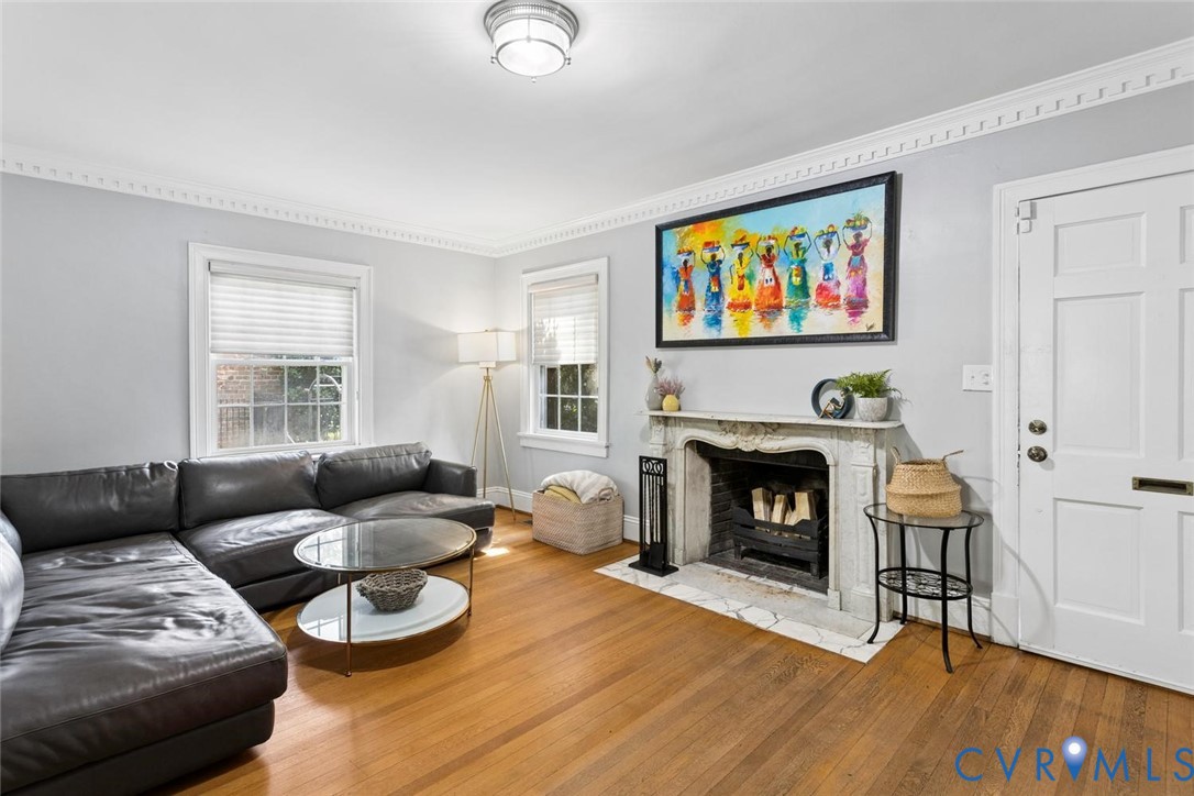Hardwood flooring, decorative crown molding, a built-in fireplace with a stone surround, white trim, and a panel door