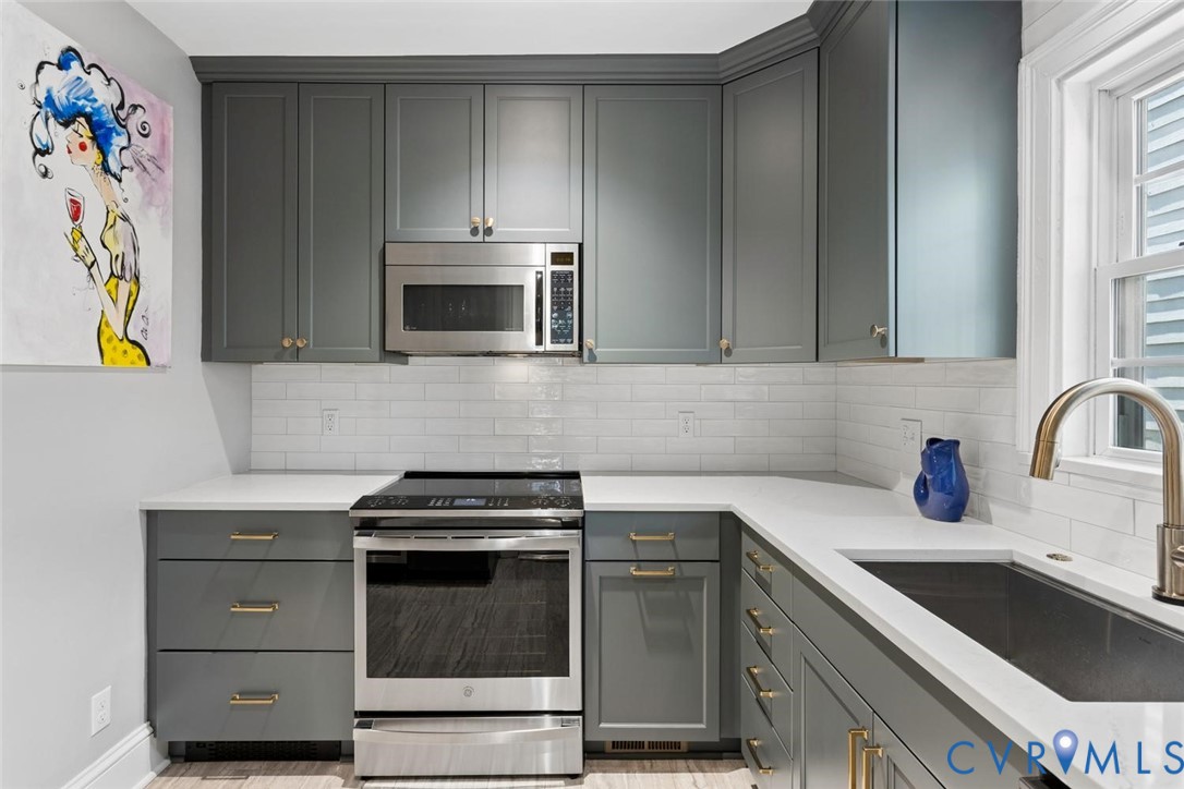 Modern kitchen featuring gray cabinetry, white countertops, subway tile backsplash, and stainless steel appliances