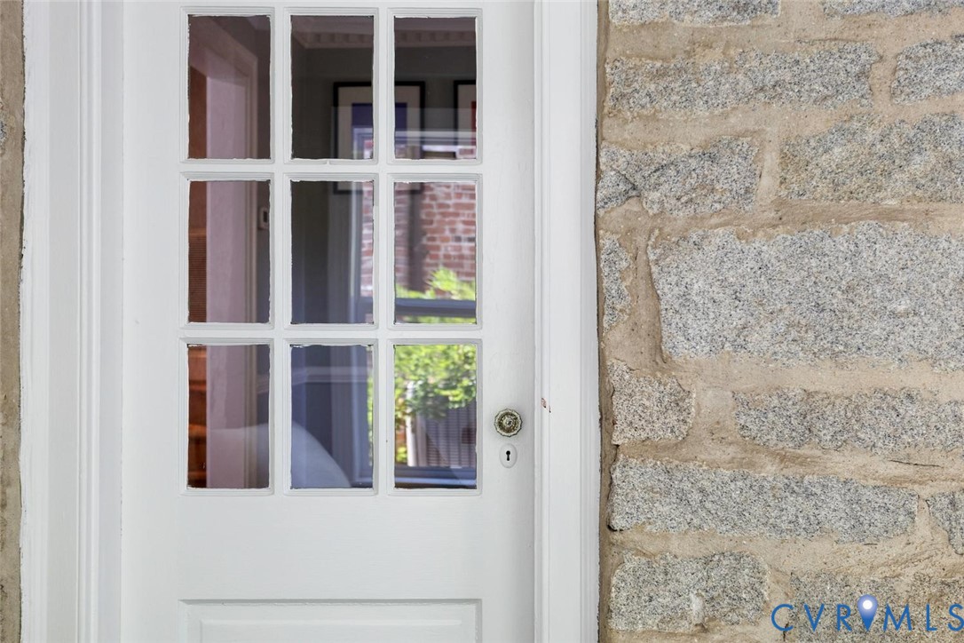 White panel door with multi-pane window, brass doorknob, and stone exterior wall