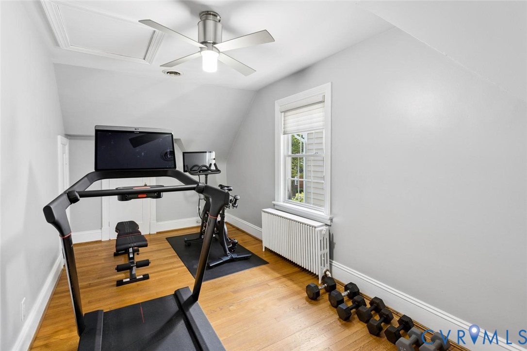 Hardwood flooring, sloped ceiling, window with blinds, ceiling fan with integrated lighting, white baseboards