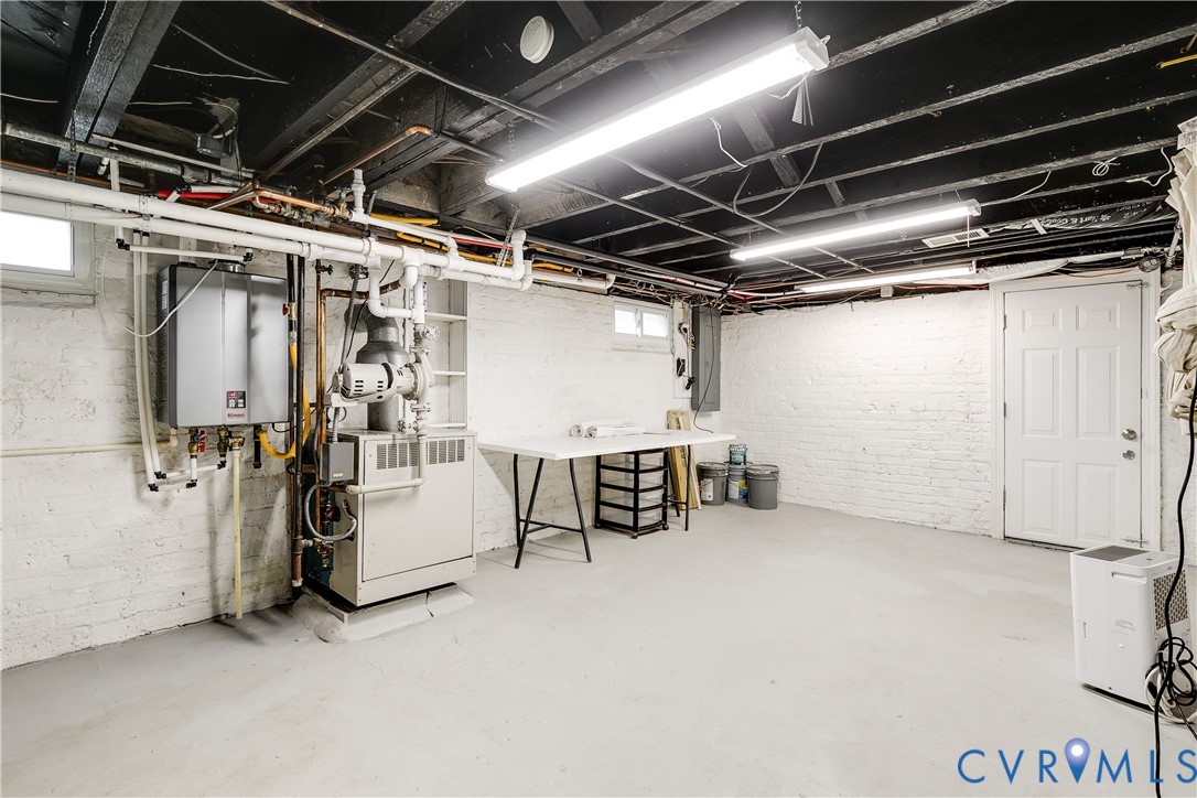 Spacious utility area featuring painted brick walls, exposed ceiling joists, and a solid core door