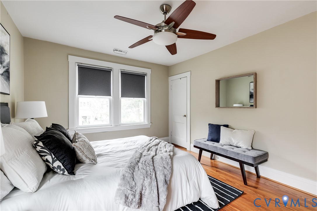 Hardwood flooring, dual windows with roller shades, white trim, and a ceiling fan with light fixture