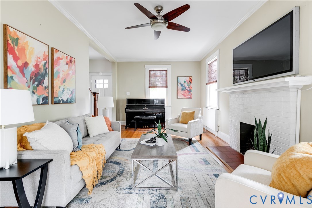 Hardwood flooring, painted brick fireplace, crown molding, and ceiling fan