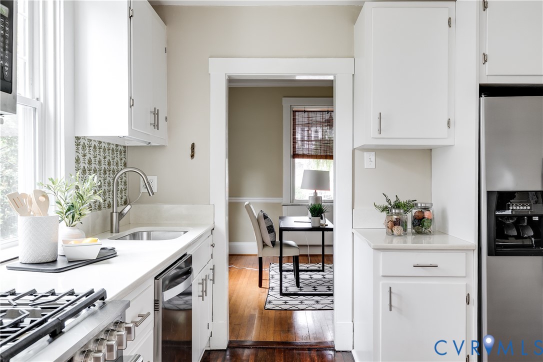 White cabinetry with brushed nickel hardware, light-toned countertops, stainless steel sink with gooseneck faucet, and a stainless steel refrigerator