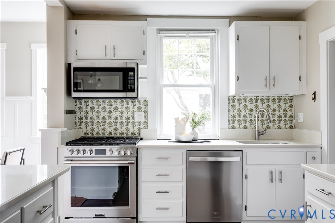Kitchen featuring white cabinetry, stainless steel appliances, patterned backsplash, solid surface countertops, and a single basin sink