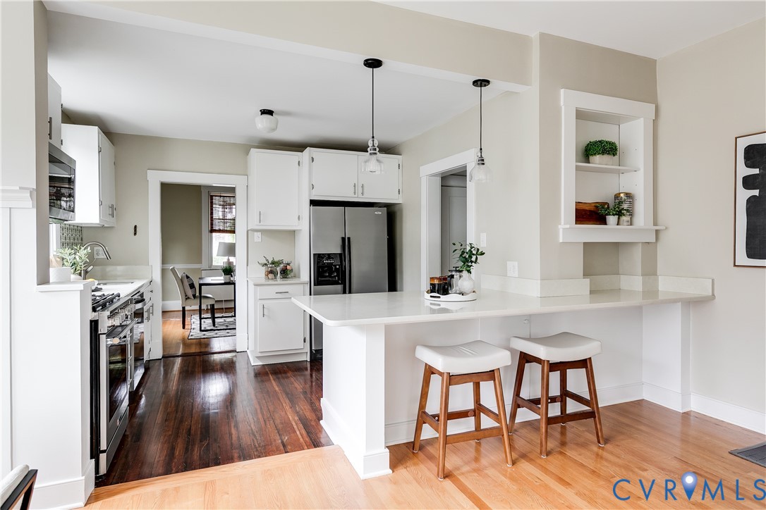 Kitchen featuring white cabinetry, stainless steel appliances, a white countertop island with seating, and pendant lighting