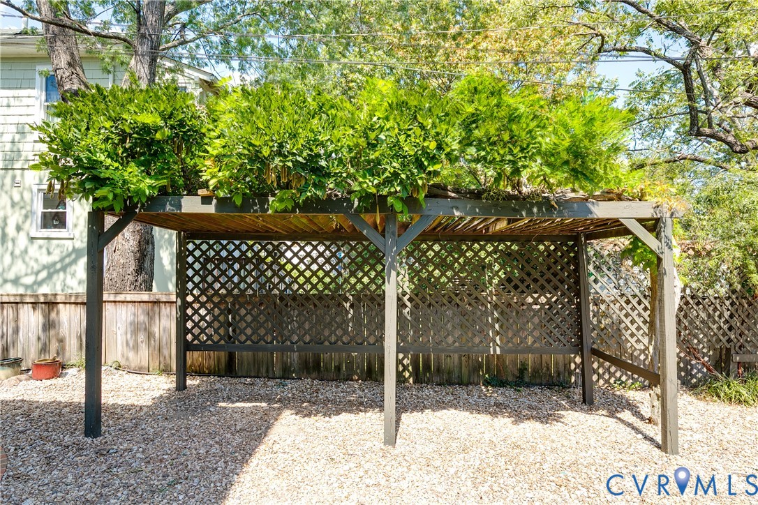 Pergola structure with lattice detailing, topped with lush greenery, set on a gravel surface
