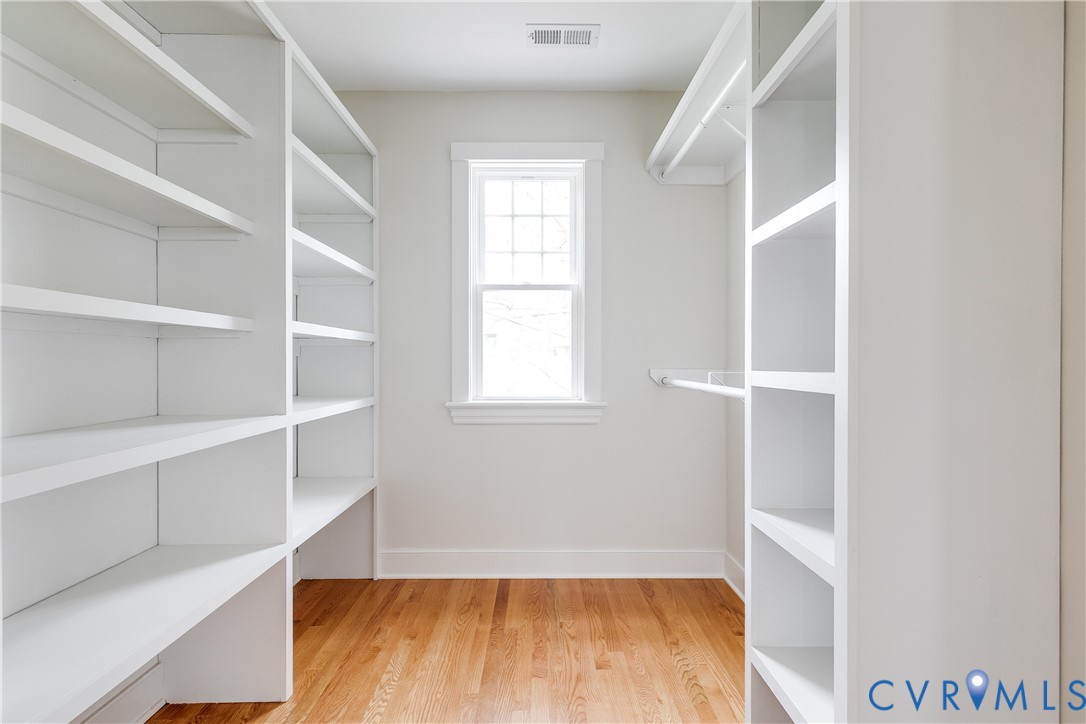 Built-in shelving, hanging rods, wood flooring, and natural light from a double-hung window