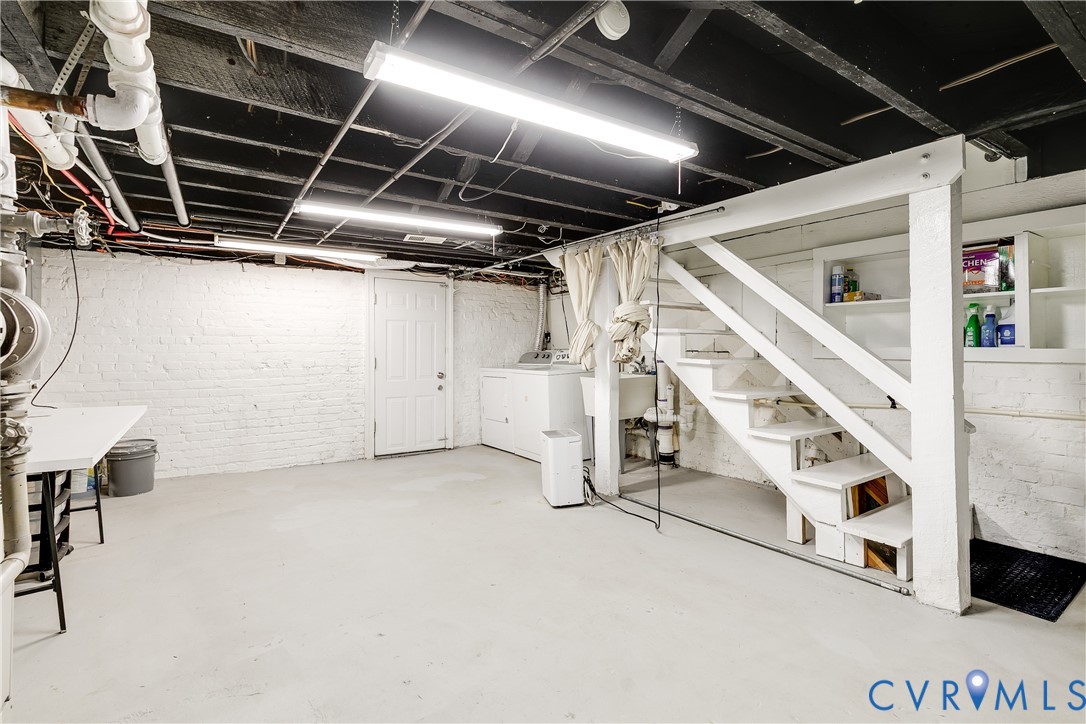Utility basement space featuring exposed ceiling joists, white painted brick walls, a built-in staircase, and a utility sink