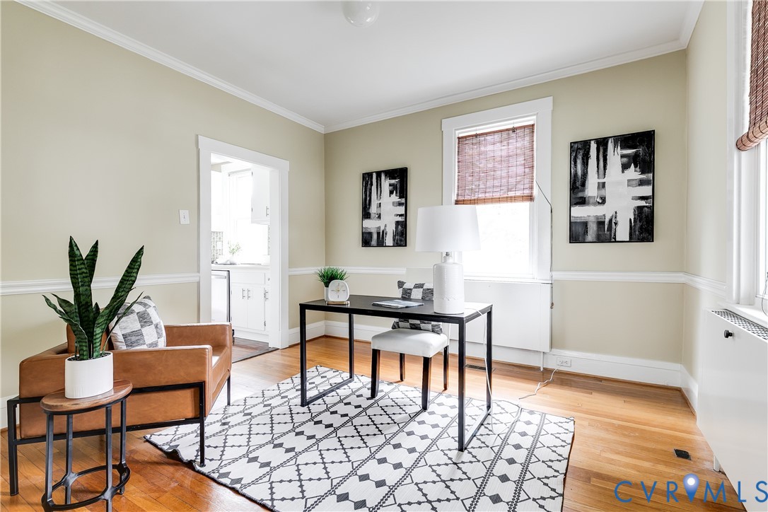 Bright, light-filled home office featuring hardwood flooring, cream and soft yellow walls with chair rail molding, and large multi-pane windows with roman shades