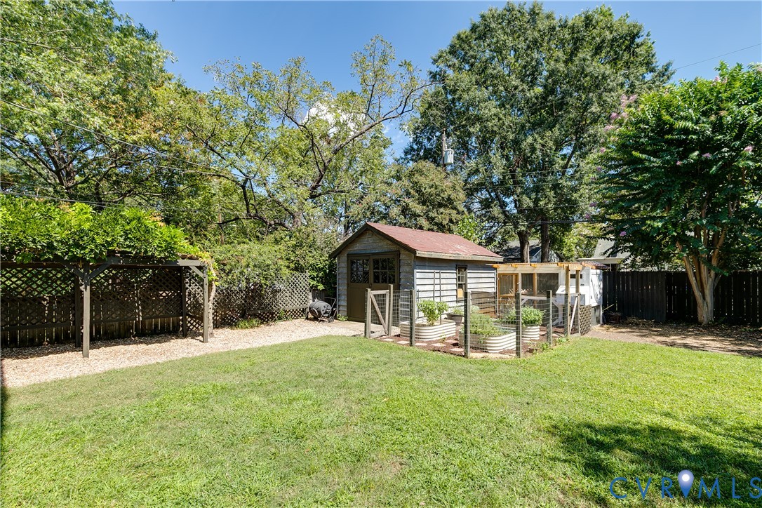 Expansive backyard featuring a lush lawn, a detached storage shed, raised garden beds, a trellis structure, and privacy fencing