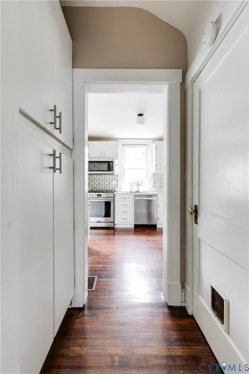 Expansive hardwood flooring extending into kitchen, white kitchen cabinetry, pantry storage and stainless steel appliances