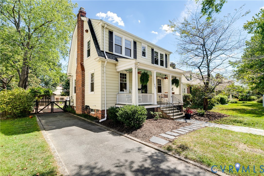 Traditional two-story residence with a covered front porch, a prominent brick chimney, and a paved driveway leading to a gated area Traditional two-story residence with a covered front porch, a prominent brick chimney, and a paved driveway leading to a gated area