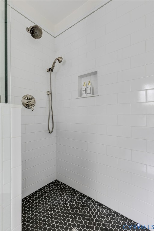 Shower featuring white subway tile walls, black hexagonal floor tile, a built-in recessed niche, and a brushed nickel showerhead with a handheld sprayer