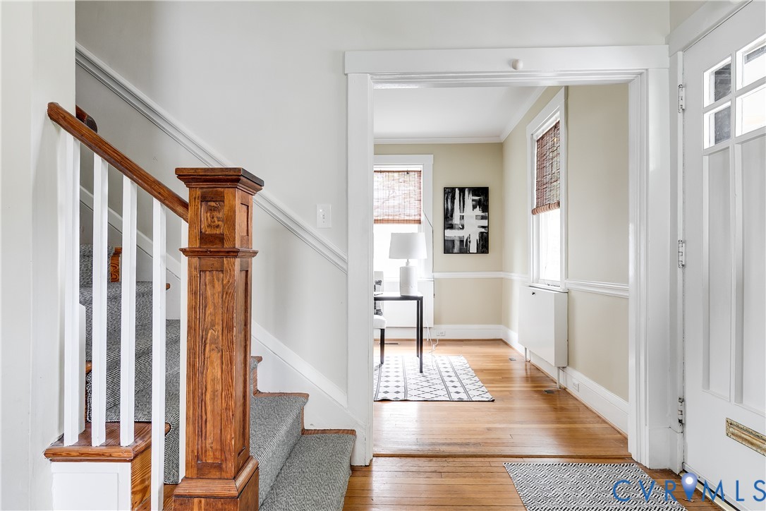 Hardwood flooring, painted trim, paneled interior door, wood newel post, and carpeted staircase