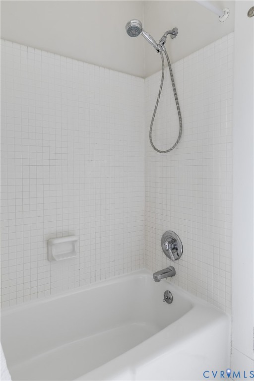 Bathtub and shower combination with white tile surround, chrome fixtures, and a hand-held showerhead
