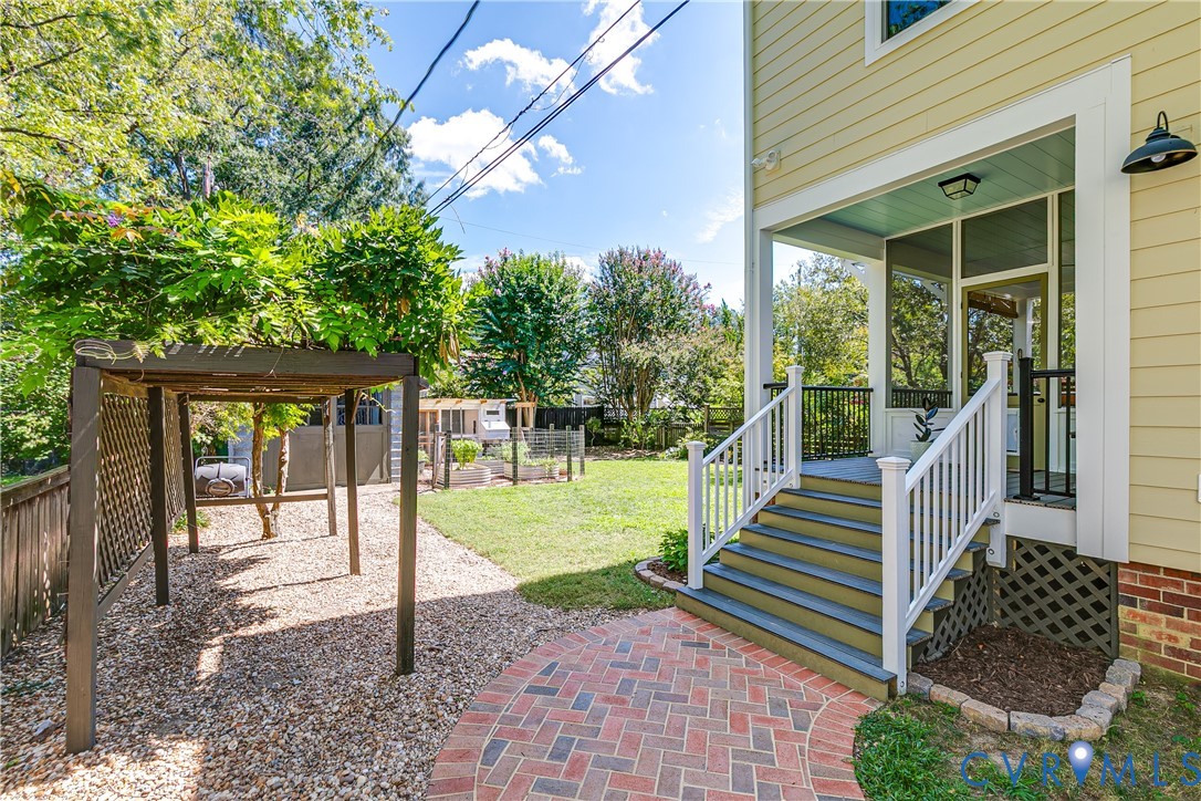 Screened porch with light blue ceiling, wood pergola, brick paver path, gravel landscaping, and green lawn area