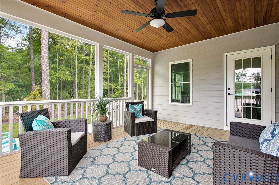 Screened porch featuring a natural wood plank ceiling, outdoor ceiling fan, light gray horizontal siding, and natural wood plank flooring