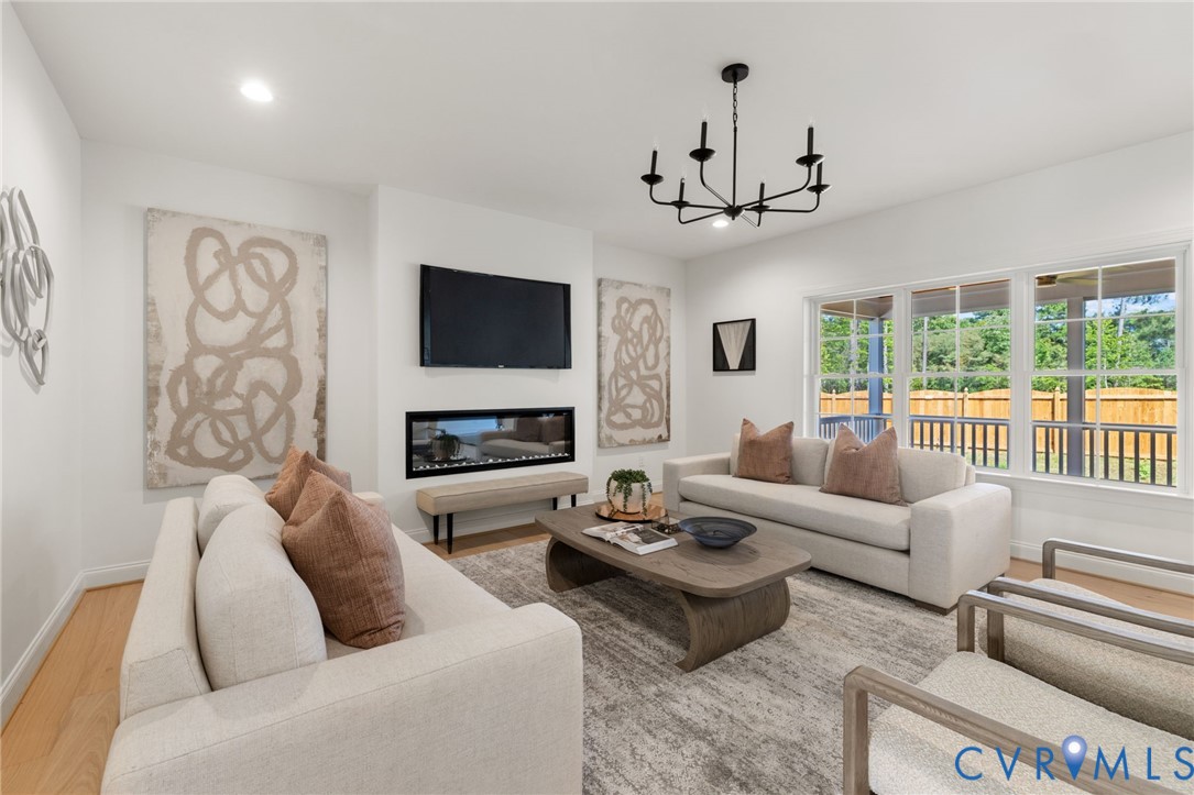 Recessed lighting illuminates the room, featuring a modern chandelier, wood-finish flooring, a linear fireplace, and multiple windows