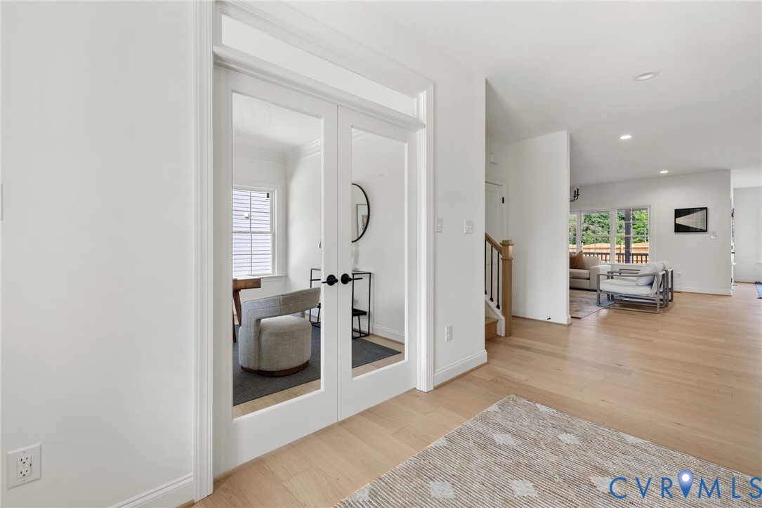 Glass-paneled double doors, light wood-finish flooring, recessed lighting, and a staircase with wood newel post and wrought iron balusters