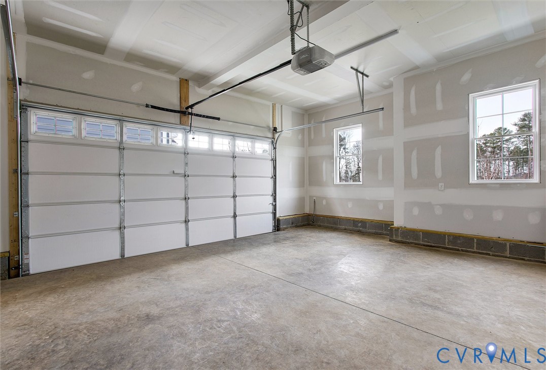 Concrete flooring, white panel garage door with upper lites, two double-hung windows, automatic garage door opener, and unfinished drywall
