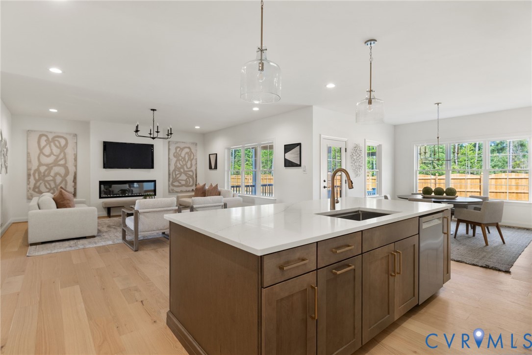 Open-concept living space featuring wood-finish flooring, a kitchen island with stone countertops, a linear fireplace, and extensive windows