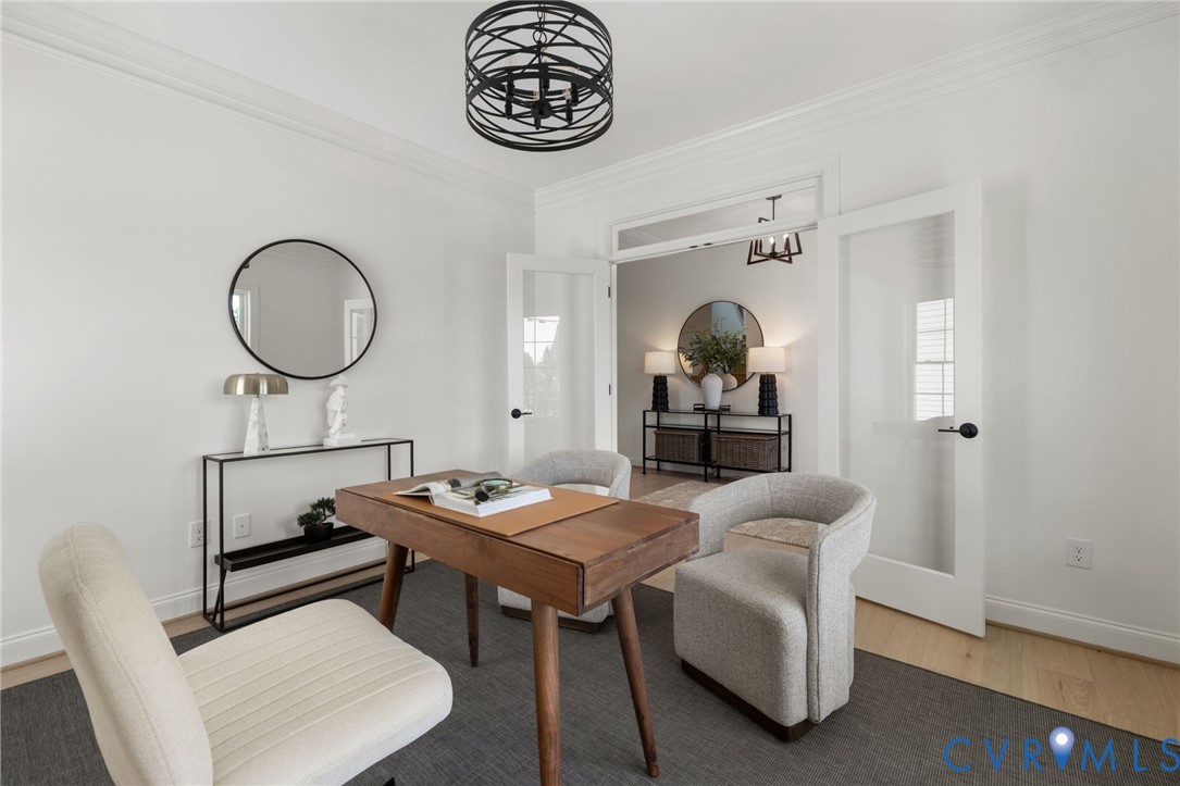 White walls with crown molding, wood-finish flooring, a contemporary black metal chandelier, and a pair of white French doors with frosted glass panels