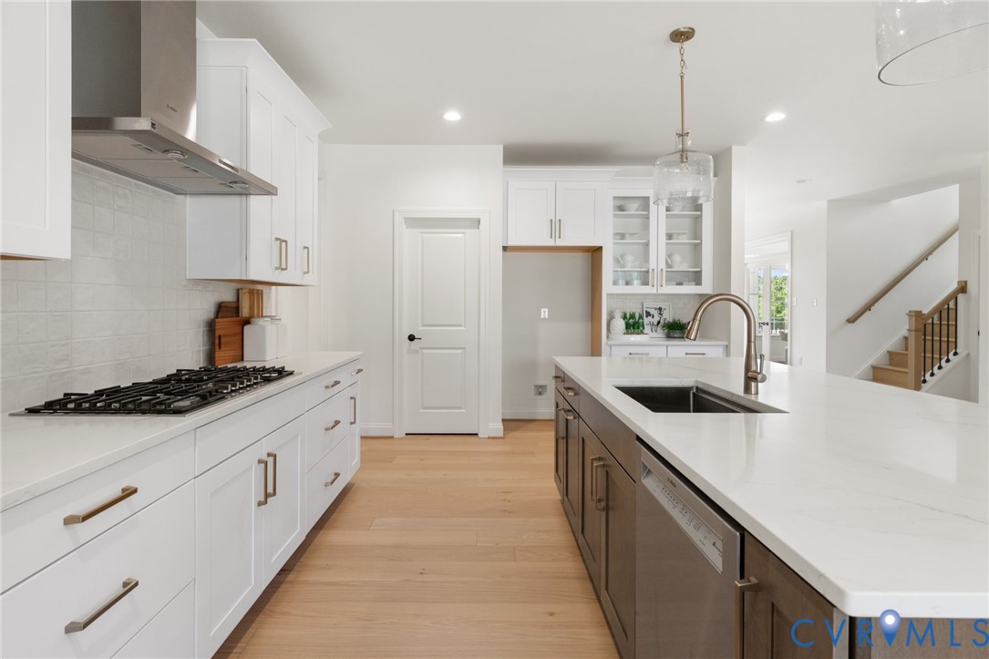 White cabinetry, large center island with built-in sink, wood-finish flooring, recessed lighting, and stainless-steel appliances