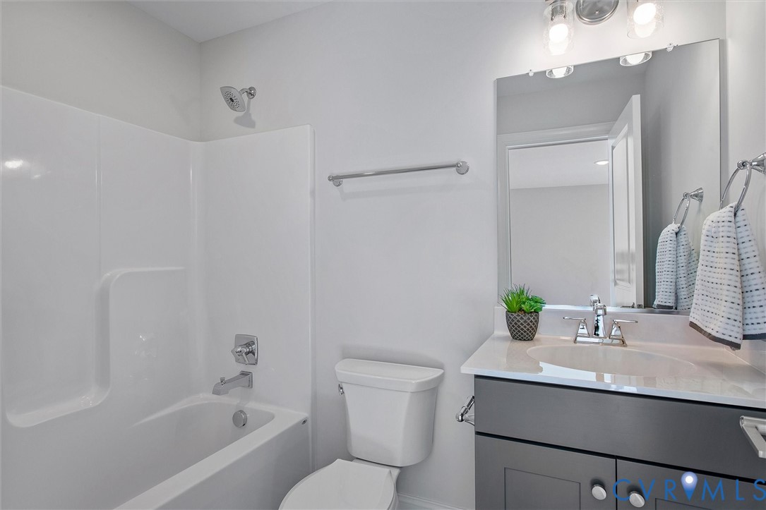 White tub/shower combination, polished chrome fixtures, rectangular vanity mirror, gray vanity cabinet, and white countertop