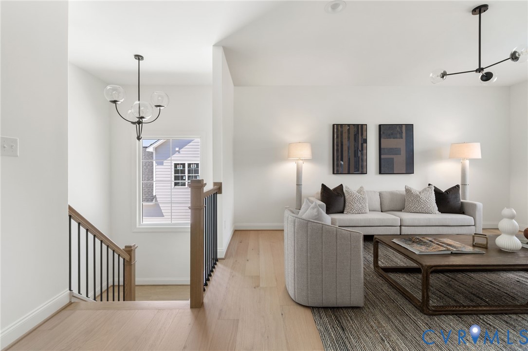 Hardwood flooring throughout, modern black and clear glass chandeliers, white walls, and a staircase with wood handrails and black balusters