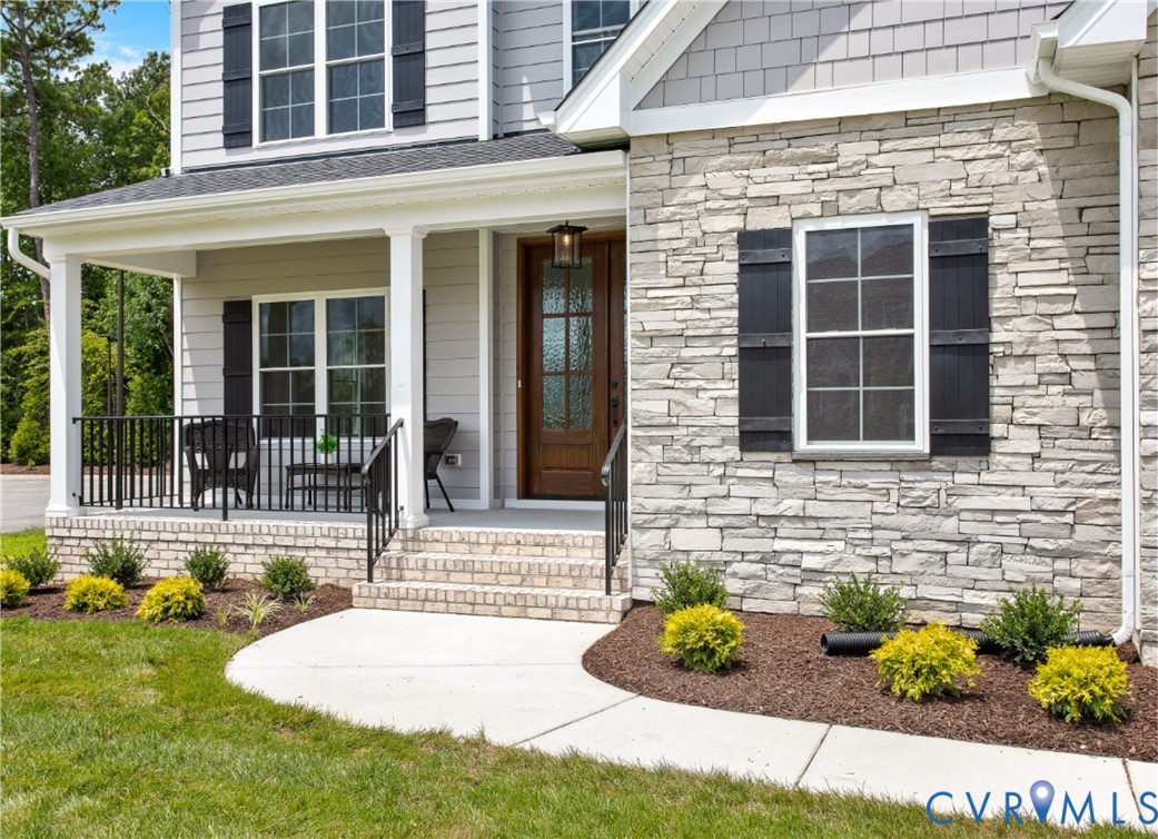 Stone veneer facade with black louvered shutters and a covered front porch featuring white columns
