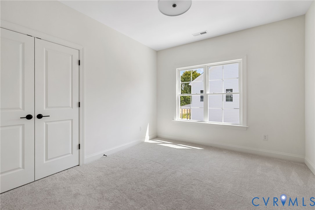 White walls with a window, light gray carpet, and white double doors with matte black hardware