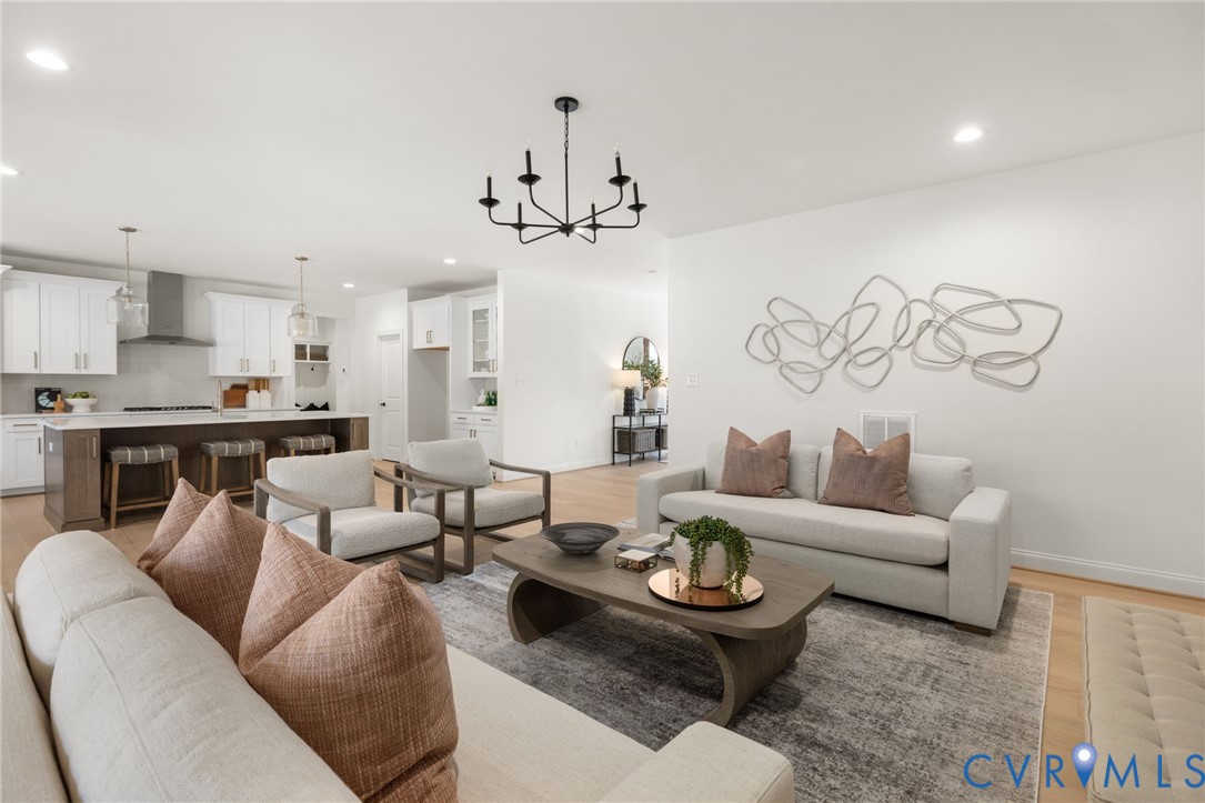 Open-concept living space featuring wood-finish flooring, a kitchen island with seating, white cabinetry, and a black chandelier