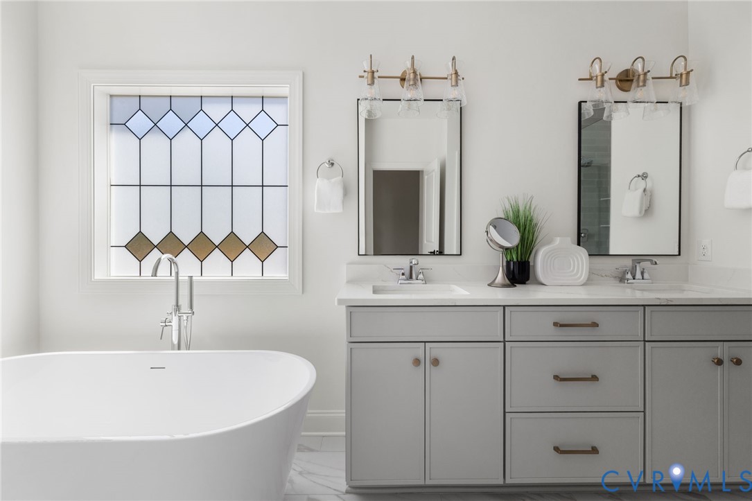 Freestanding soaking tub with chrome-finish faucet, decorative privacy window, dual vanity with undermount sinks, and wall-mounted light fixtures