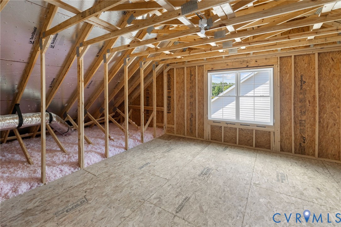 Unfinished attic space with exposed wooden trusses, a double-hung window, oriented strand board walls, and subflooring