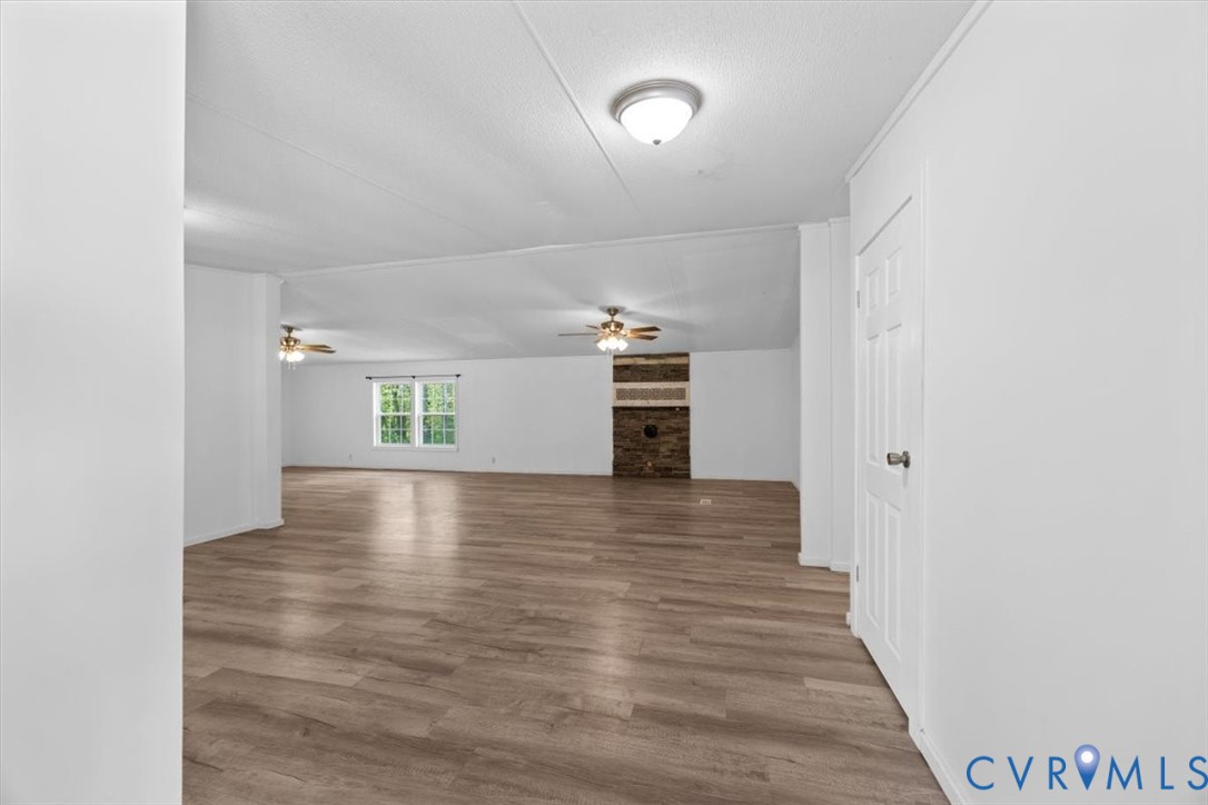 Open-concept interior featuring wood-finish flooring, a masonry fireplace, ceiling-mounted light fixtures, dual ceiling fans, and a six-panel door